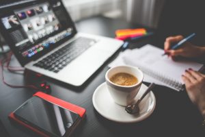 A person writing in a notebook in front of a laptop.