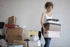 girl carrying boxes in a messy room trying to declutter before moving from Florida to California
