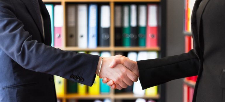 Two people in suits shaking hands in an office.