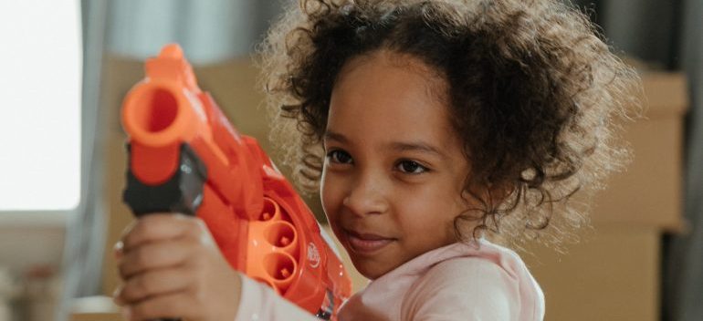 A girl with a plastic gun playing in a moving box