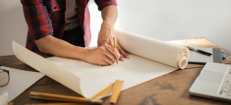 a table with a paper and man drawing a design on it 