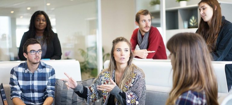 A group of young people seating and standing in the room discussing the conditions of the office move