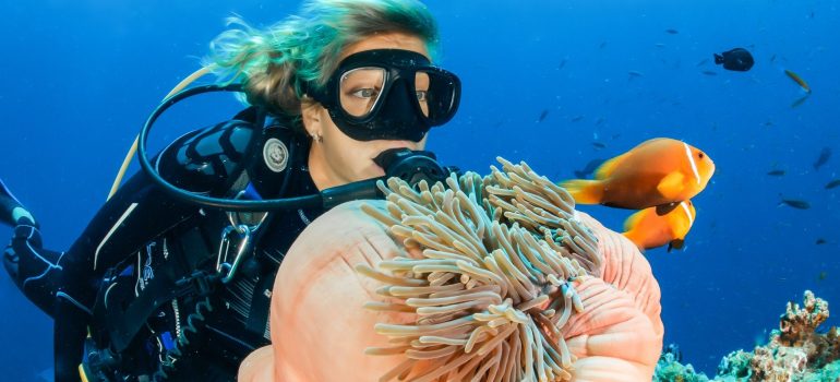 A woman with mask and in diving suite watching a piece of the coral reef with fishes swimming around her