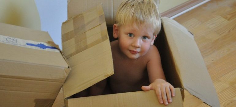 A boy sitting in a cardboard box to representing moving from Kendall to Pompano Beach