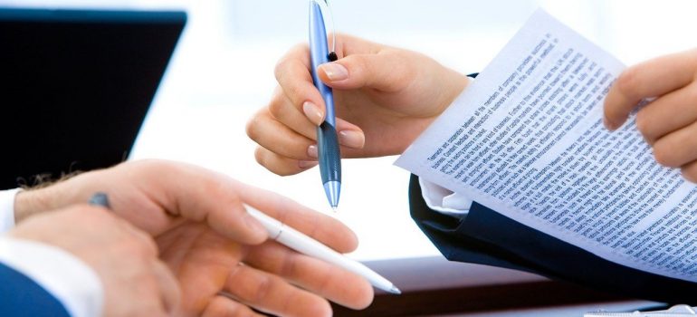 Two hands holding pens and papers with typed letters, preparing to sign them. 