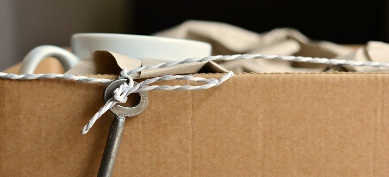 The rim of a cardboard box with a key on a string, a mug and a cloth peeking out from it