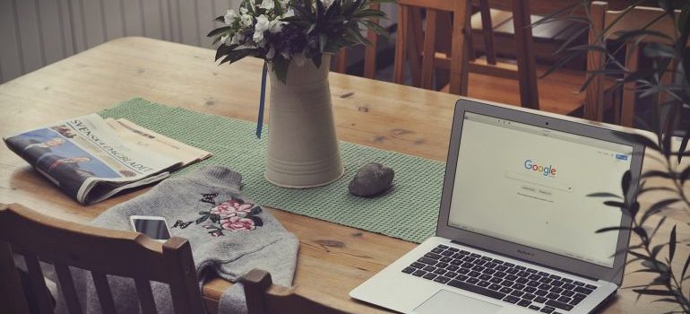 A laptop on a dining table with a flower vase and a newspaper - finding professional movers on short notice 