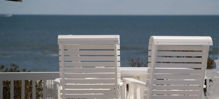 Two white chairs on the balcony with a view to the ocean. 