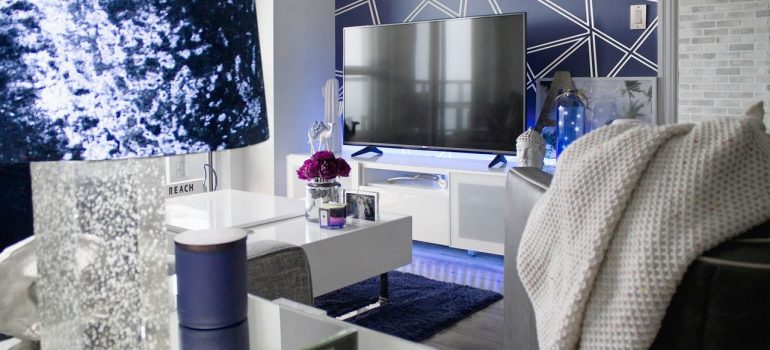Modern flat with blue and silver details, flat TV, table with glass vase, blue cup, and small vase with flowers, you will see when renting a flat in Boca Raton. 