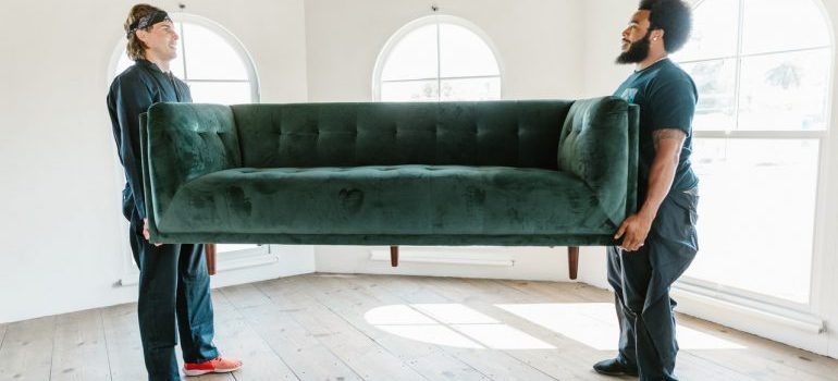 Two man lifting up a sofa unprotected which is why you shouldn't hire unlicensed movers.