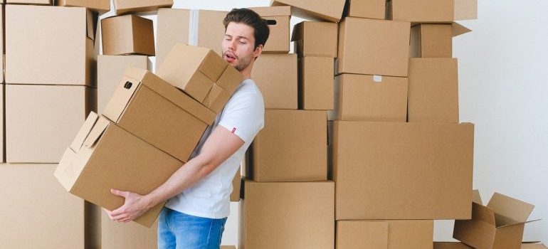 A man carrying cardboard boxes stacked one on top of another, with a lot of boxes behind him as well representing where to store possessions while renovating a home in Fort Lauderdale