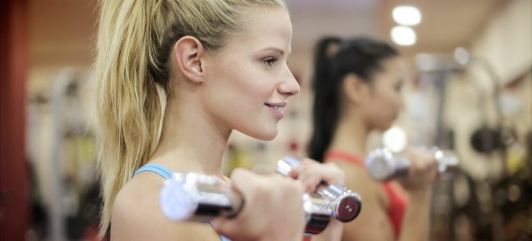 Two girls with ponytails are exercising in the gym with hand weights.
