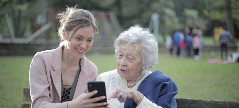 elderly woman and a young woman sitting on a bench looking at a smartphone