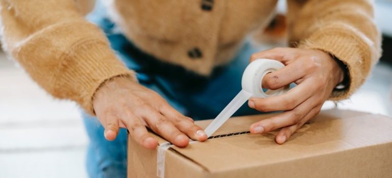 Person duct taping a cardboard box.