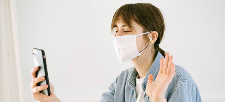 A woman is wearing mask and looking at the phone in orde to throw a safe housewarming party