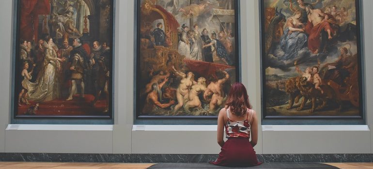 woman sitting in front of three paintings in a museum