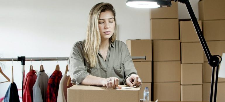 A woman thinking about ways to reduce your costs of moving to Miami while putting a sticker on the box. 