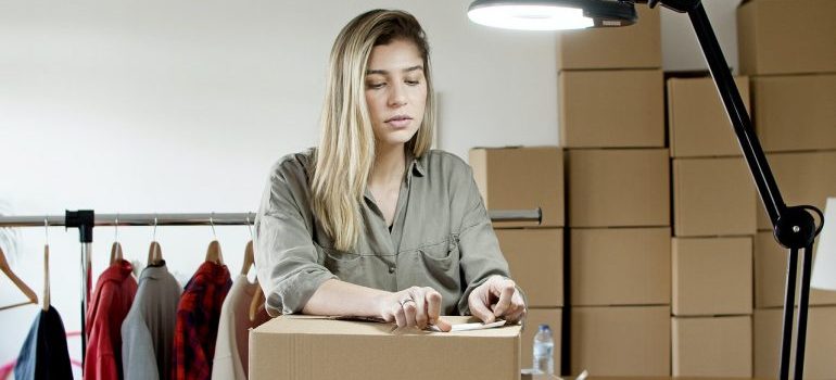 A woman thinking about ways to reduce your costs of moving to Miami while putting a sticker on the box.