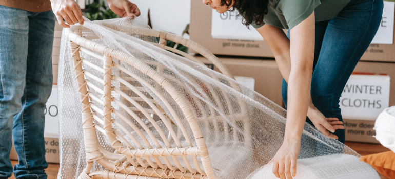 a couple placing bubble wrap over a wooden chair before packing it for local movers Jupiter FL to relocate it