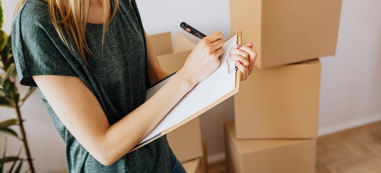 woman taking notes in clipboard near carton boxes befor going to Inspect a potential home before buying