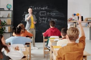 Teacher in the classroom with kids raising hands - good school is important when moving to Miami