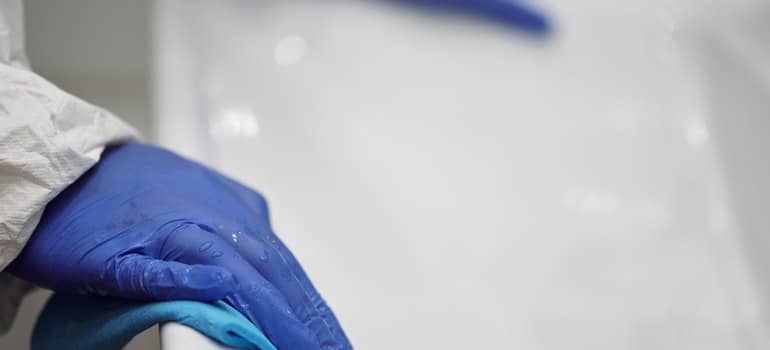 hands in blue gloves cleaning a white tub