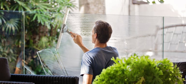 Man in gray shirt cleaning clear glass wall near sofa