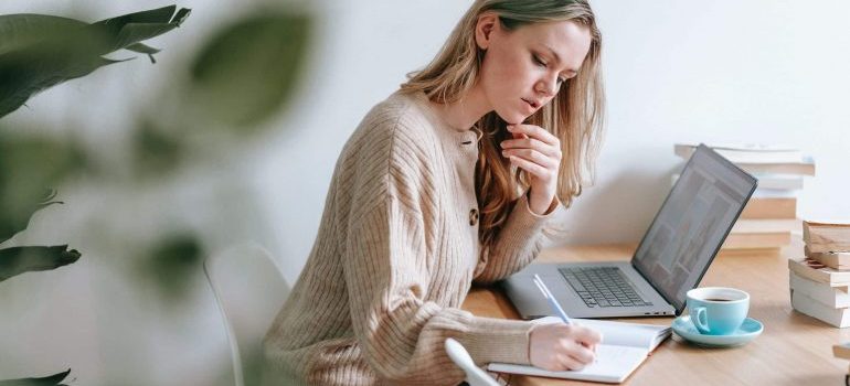 A woman doing research on her laptop and writing about how to deal with stress when moving to Fort Lauderdale