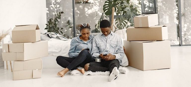A couple who know the cheapest way to move between the states with packed boxes for moving sitting on the floor.
