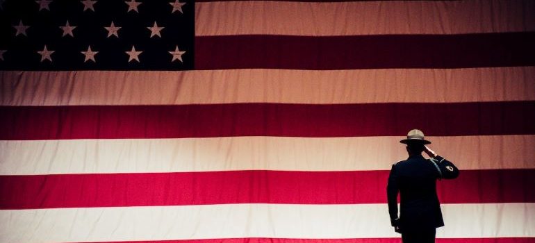 A military personnel standing in front of the flag of USA.