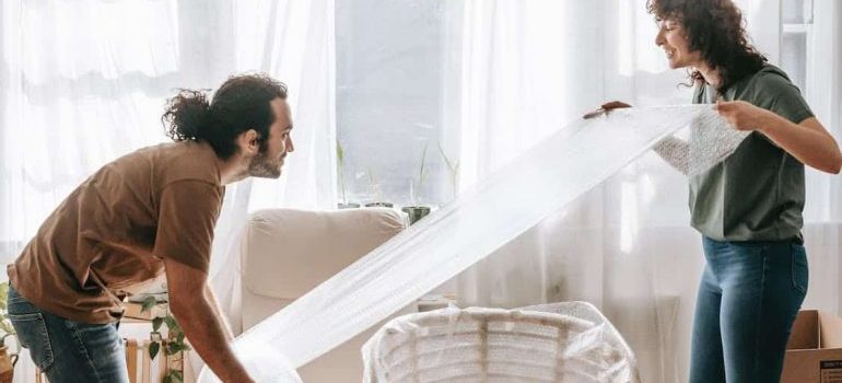 A man and a woman using a bubble wrap for packing a chair.