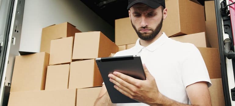 A man from a moving company taking some notes on a sheet of paper in front of moving boxes.