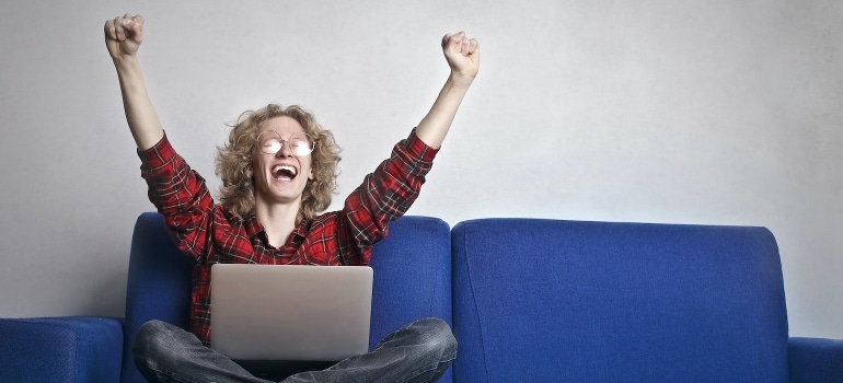 An excited person with hands up sitting on a blue sofa. 