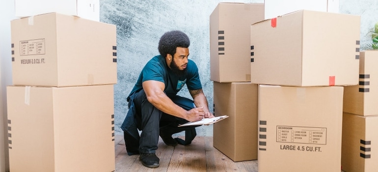 A man crouching, looking at boxes and working on moving from Florida to California