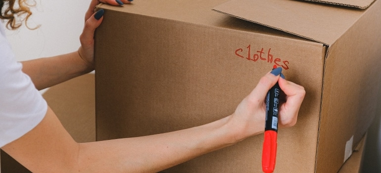 A woman labels moving boxes with a marker.