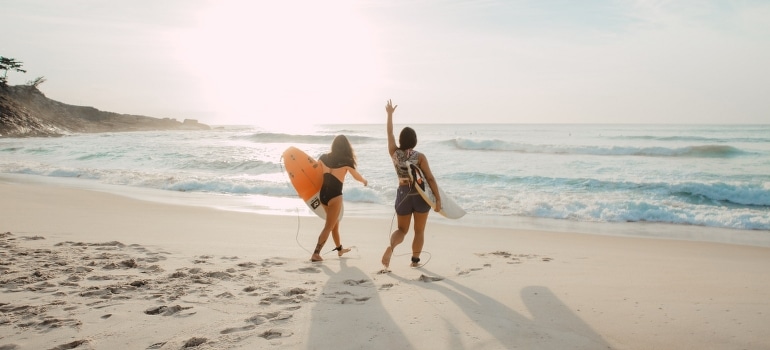 Two women walking by the beach carrying surfboards and looking forward to moving from Fort Lauderdale to West Palm Beach