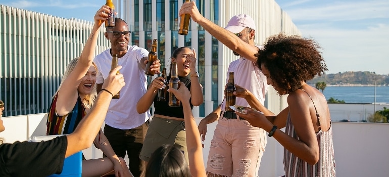 Joyful friends toasting with beer and trying to deal with stress when moving to Miami.