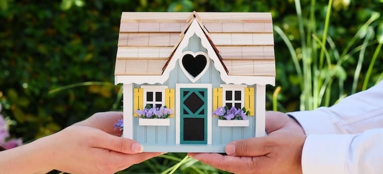 People holding miniature wooden house