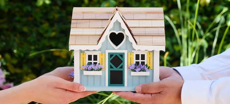 Two people holding a wodden miniature house