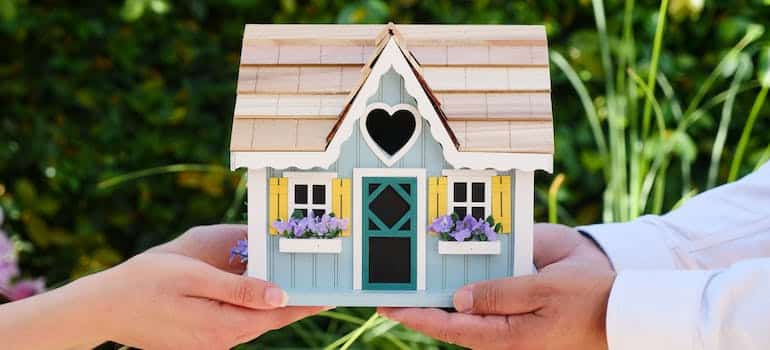 Two people holding a wodden miniature house 