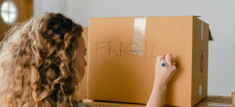 A woman writing fragile on the box